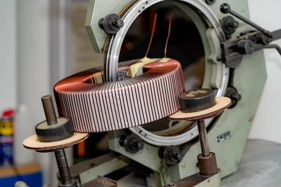 Toroidal transformer being wound on an industrial coil-winding machine: precision copper turns around a large toroidal core